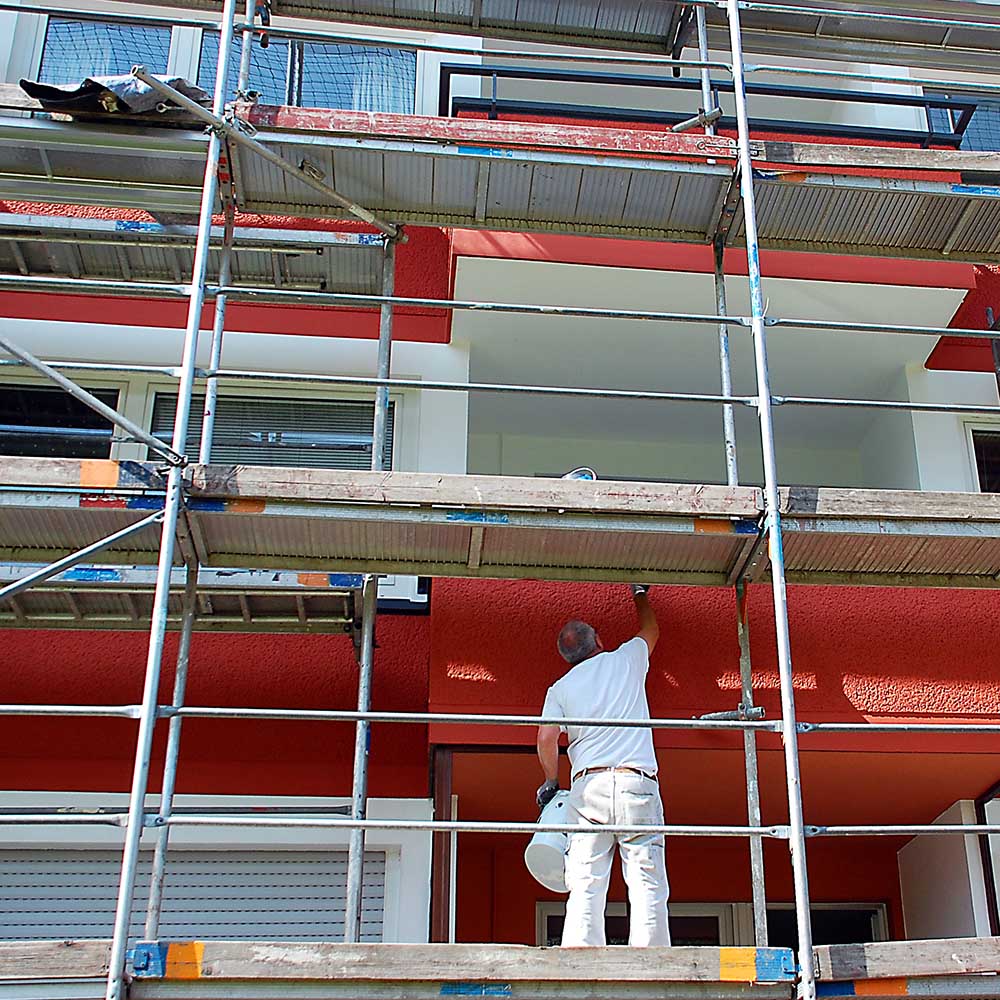 Maler auf Gerüst streicht die Außenfassade eines Mehrfamilienh